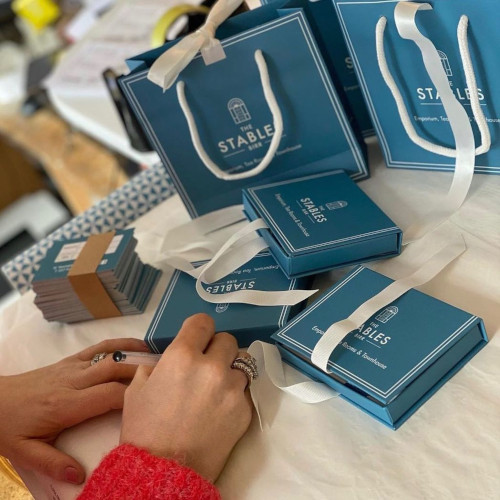 various blue gift boxes on a table with a person writing in a card